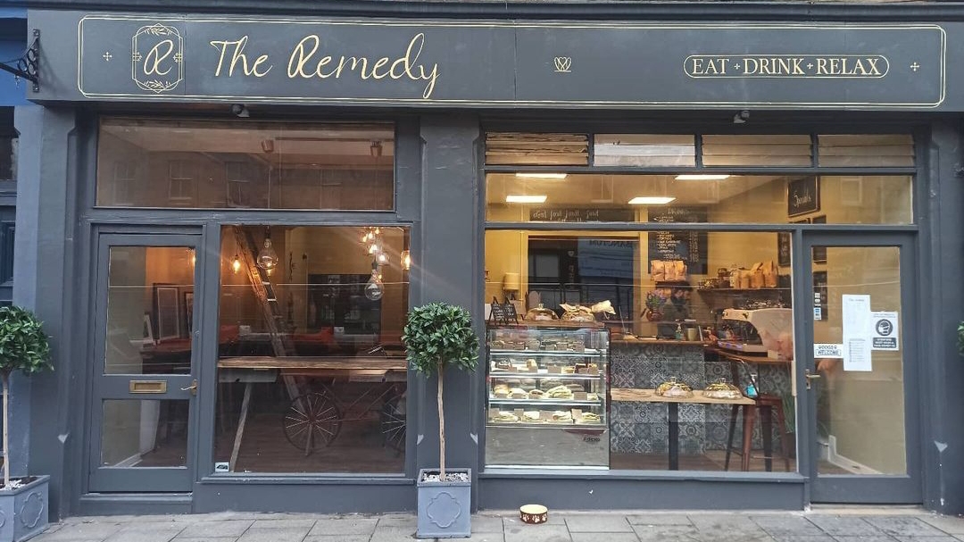 The charcoal shopfront with The Remedy in gold script, an ornate R monogram, and Eat Drink Relax lettering.