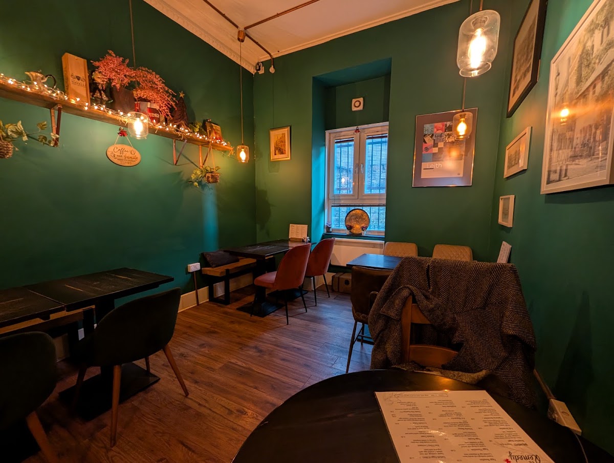 The green-walled back room: Edison pendants, fairy lights along a shelf, rust velvet chairs, a tweed throw and framed prints of Leith.