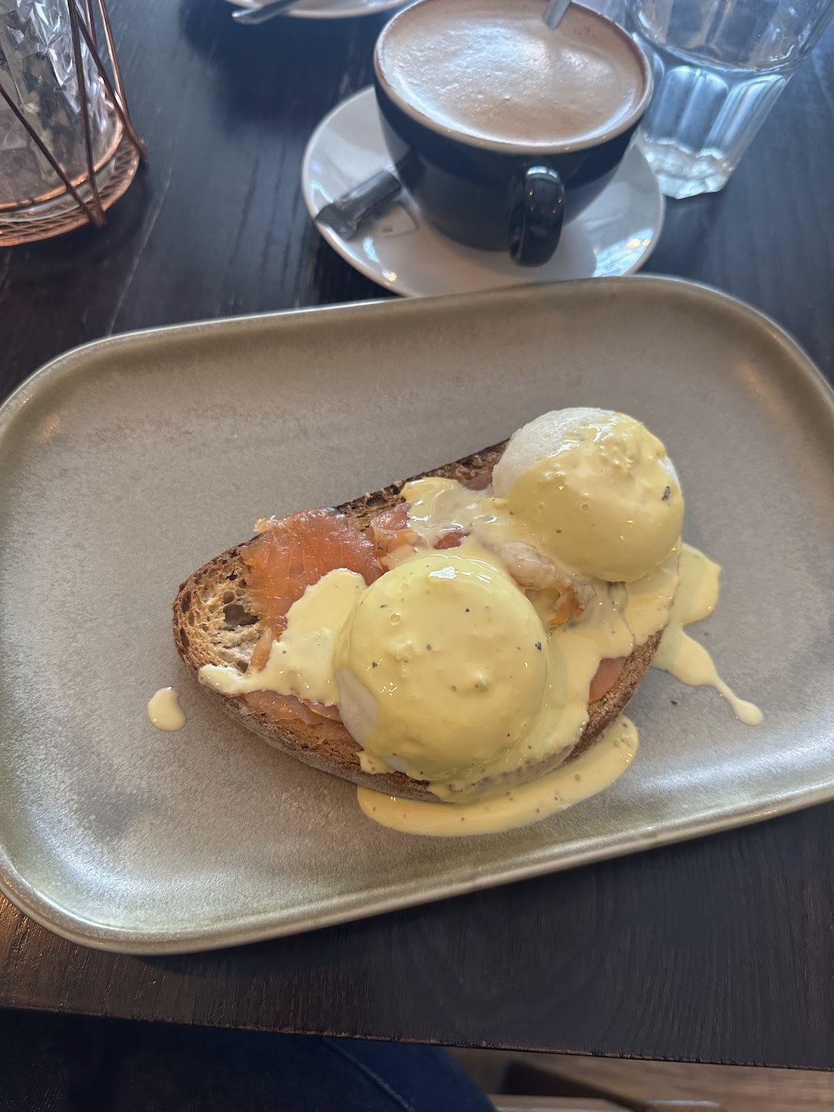 Poached eggs and smoked salmon on toasted sourdough under hollandaise, with a flat white behind.